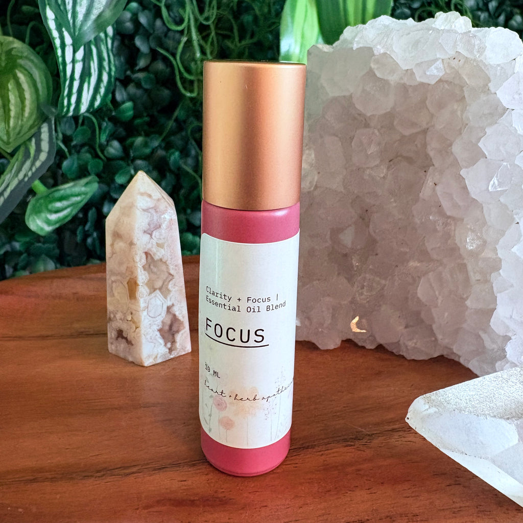Roll-on bottle labeled 'Focus' with a gold cap and white label on a wooden surface with crystals and plants in the background.